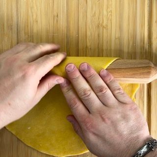 Una persona sta stendendo un pezzo di pasta su un tagliere di legno.