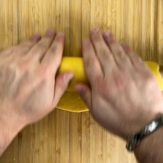 Una persona tiene in mano un pezzo di pasta gialla su un tagliere di legno.