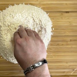 La mano di una persona sta infilando la mano in un mucchio di farina su un tavolo di legno.