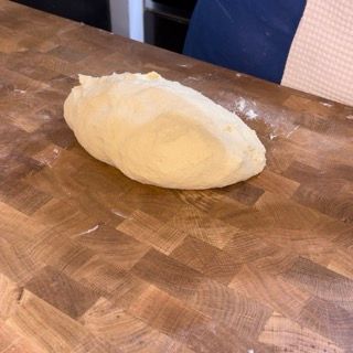 Una palla di pasta è appoggiata su un tagliere di legno.