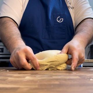 Un uomo con un grembiule blu sta impastando la pasta