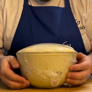 Un uomo con un grembiule tiene in mano una ciotola di pasta