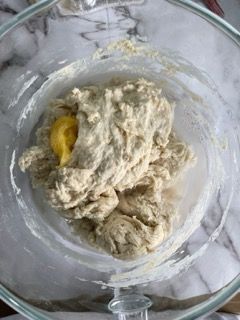 Una ciotola di vetro piena di impasto e un uovo dentro.