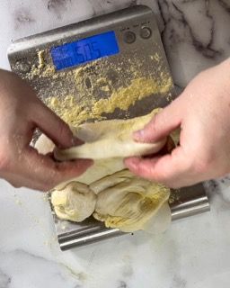 Una persona tiene in mano un pezzo di pasta su una bilancia.