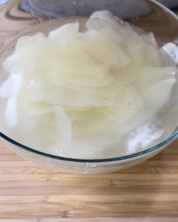 Una ciotola di vetro piena di patate a fette su un tavolo di legno.