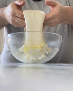 Una persona tiene in mano un pezzo di impasto in una ciotola di vetro.