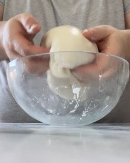 Una persona tiene in mano una palla di pasta in una ciotola di vetro.