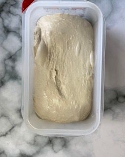 Un contenitore di plastica pieno di impasto è appoggiato su un bancone di marmo.