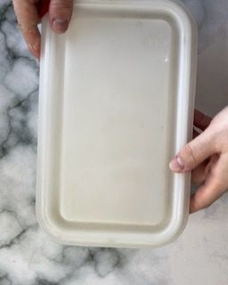 Una persona tiene in mano un contenitore di plastica bianco con un coperchio.