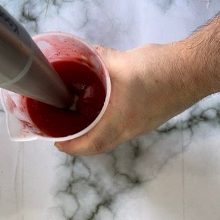 Una persona tiene in mano un misurino contenente del liquido rosso.