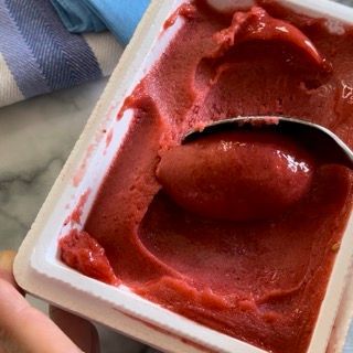 Una persona tiene in mano un cucchiaio in una scatola di gelato alla fragola.