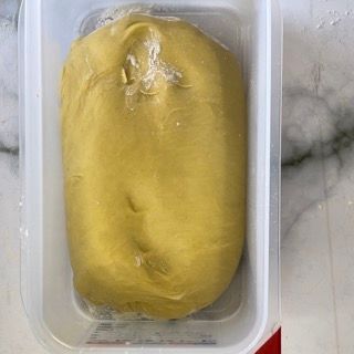 Un contenitore di plastica pieno di pasta gialla è appoggiato su un tavolo.