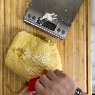 Una persona sta misurando l'impasto su un tagliere accanto a una bilancia.