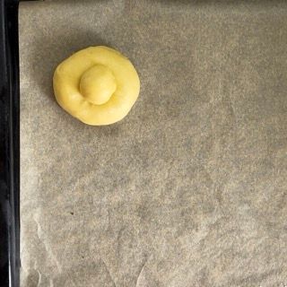 Una piccola pallina di pasta gialla è appoggiata su un pezzo di carta oleata.