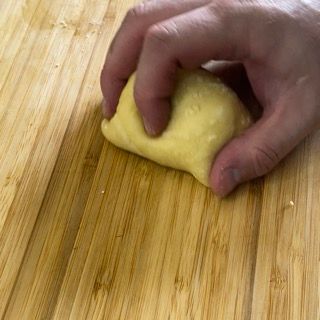 Una persona tiene in mano un pezzo di pasta su un tagliere di legno.