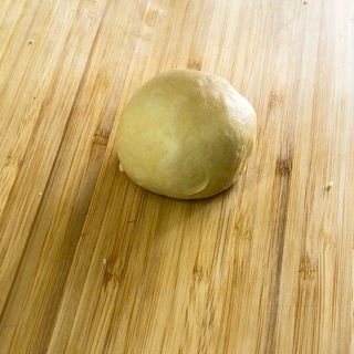 Una palla di pasta è appoggiata su un tagliere di legno.