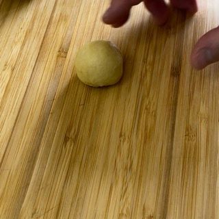 Una persona tiene in mano una palla di pasta su un tagliere di legno.