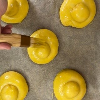 Una persona sta usando una spazzola di legno per spennellare l'impasto giallo su una teglia da forno.