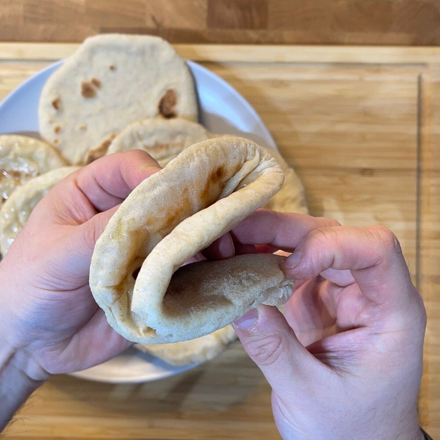 Una persona tiene in mano un pane pita davanti a un piatto di pane pita.