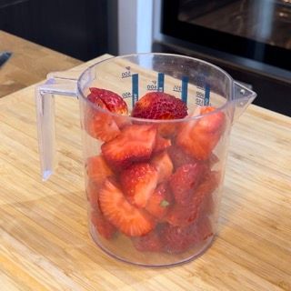 Una tazza graduata piena di fragole è appoggiata su un tagliere di legno