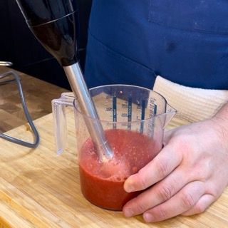 Una persona sta mescolando un liquido rosso in una tazza graduata