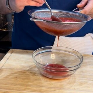 Una persona sta filtrando un liquido rosso in una ciotola di vetro