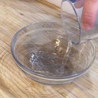 Una persona versa acqua in una ciotola di vetro su un tavolo di legno.