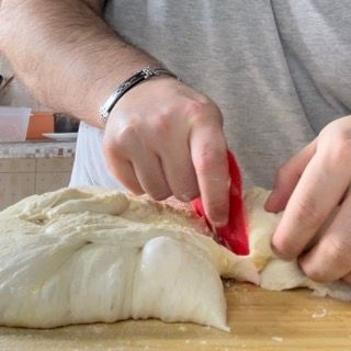 Una persona sta usando una spatola per stendere l'impasto su un tagliere