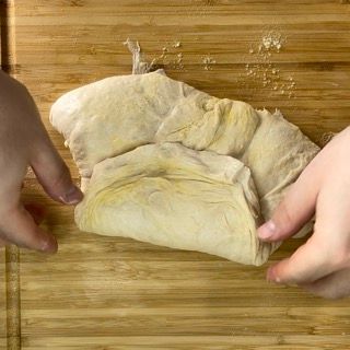 Una persona tiene in mano un pezzo di pasta su un tagliere di legno.