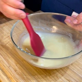 Una persona sta mescolando qualcosa in una ciotola con un cucchiaio rosso