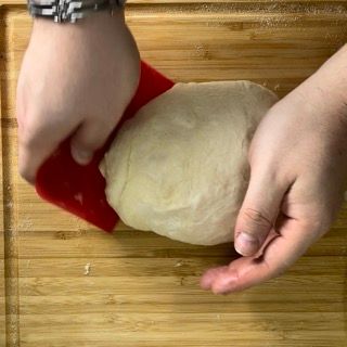 Una persona tiene in mano un pezzo di pasta su un tagliere di legno.