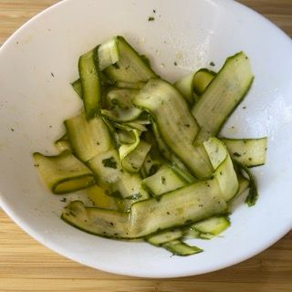 Una ciotola bianca piena di zucchine tagliate a fette su un tavolo di legno.
