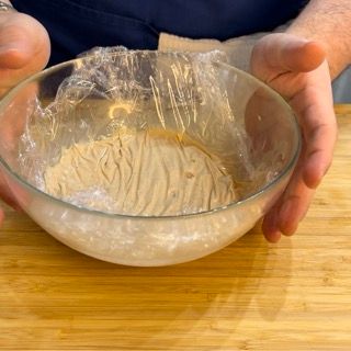 Una persona tiene in mano una ciotola di cibo avvolta nella pellicola trasparente.