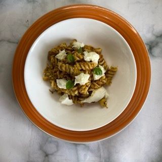 Una ciotola di pasta con formaggio e cipolle verdi su un piatto arancione