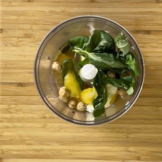 Un robot da cucina pieno di verdure e ceci su un tavolo di legno.