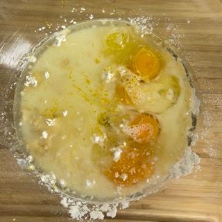 Una ciotola di vetro piena di uova e latte su un tavolo di legno.