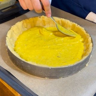 Una persona sta versando del liquido giallo in una crosta di torta con un cucchiaio