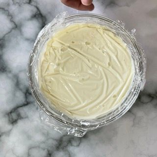 Una persona tiene in mano una ciotola di glassa avvolta nella pellicola trasparente.