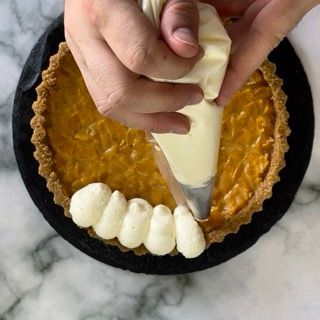 Una persona sta glassando una torta di zucca con panna montata