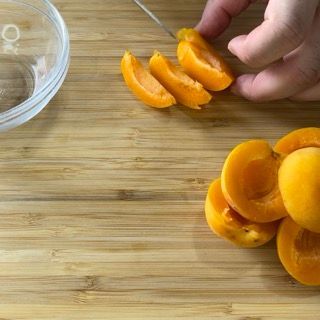 Una persona sta tagliando le albicocche su un tagliere di legno.