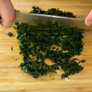 Una persona sta tagliando gli spinaci su un tagliere di legno