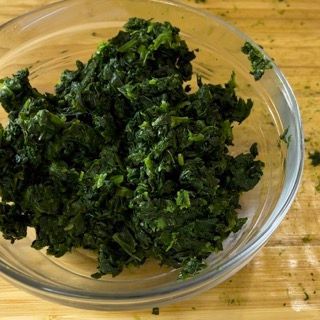 Una ciotola di vetro piena di spinaci tritati su un tavolo di legno