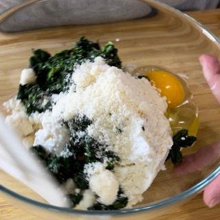 Una persona sta mescolando ingredienti in una ciotola di vetro, tra cui spinaci e formaggio