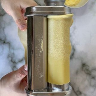 Una persona sta usando una macchina per la pasta per fare i ravioli.
