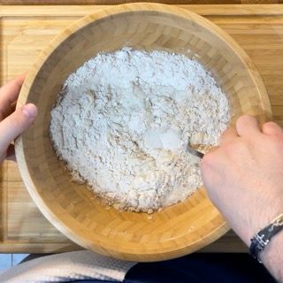 Una persona sta mescolando la farina in una ciotola di legno con un cucchiaio.