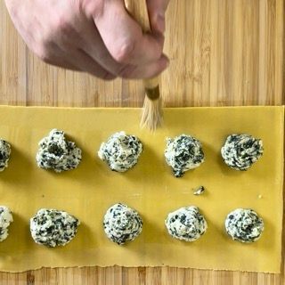 Una persona sta usando un pennello per fare i ravioli su un tagliere.