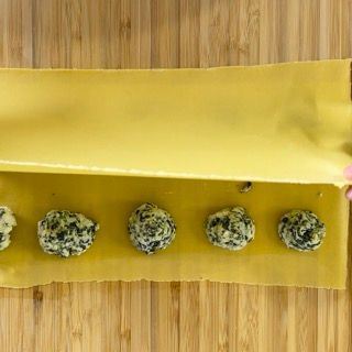 Una persona sta preparando dei ravioli con spinaci e formaggio su un tavolo di legno.