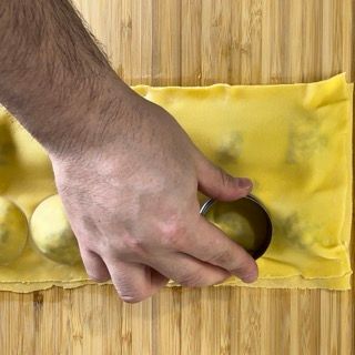 Una persona sta tagliando un pezzo di pasta su un tagliere di legno.