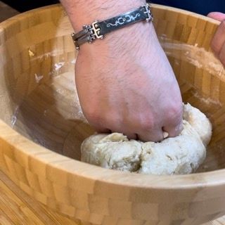 Una persona che indossa un braccialetto sta impastando l'impasto in una ciotola di legno