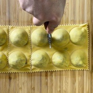 Una persona sta tagliando i ravioli su un tagliere di legno
